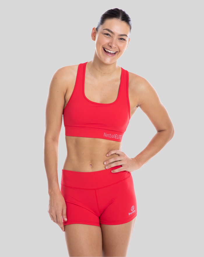 A woman wearing a red sports crop top and shorts, standing against a white background.